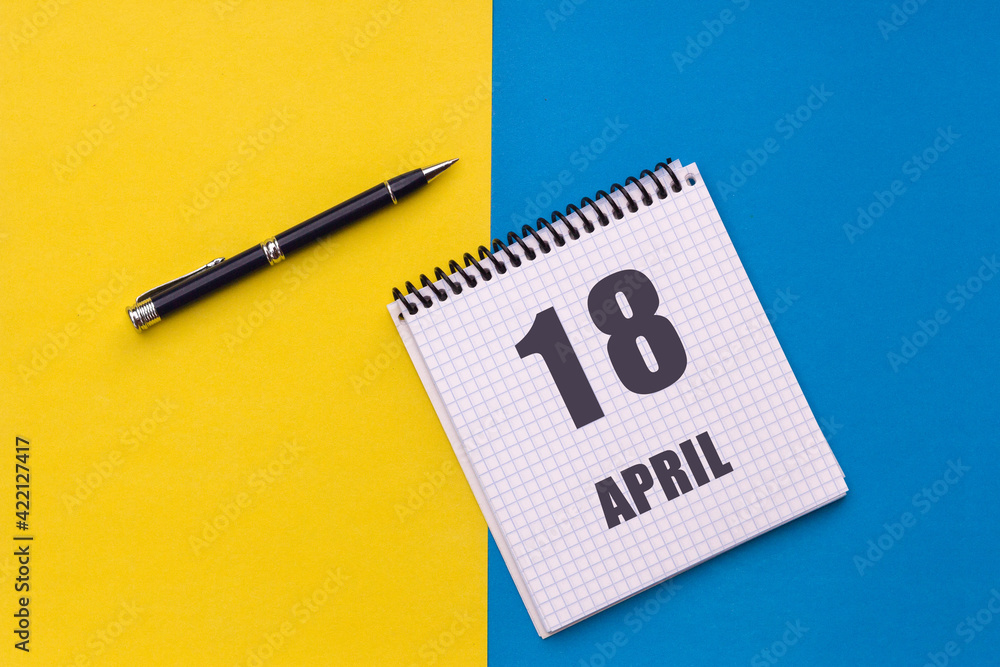 April 18th. Day of 18 month, calendar date. A notebook with a spiral and a pen lies on a yellow-blue background, flat lay, copy space April 18th. Day of 18 month, calendar date. A notebook with a spiral and a pen lies on a yellow-blue background, flat lay, copy space