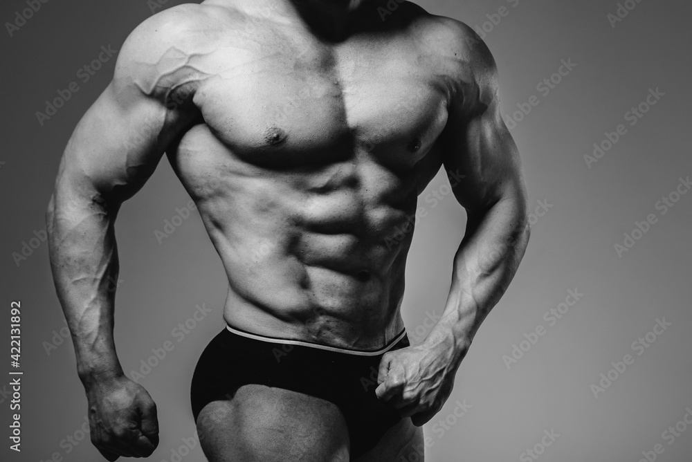 A young athlete bodybuilder poses in the studio topless, showing off his abs and muscles. Black and white. A young athlete bodybuilder poses in the studio topless, showing off his abs and muscles. Black and white.