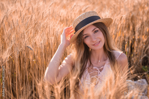 Young blonde woman in straw hat on the background of a field of golden spikelets of wheat, rye. Close-up portrait of beautiful girl with brown eyes. Weekend walk outside the city. Agricultural texture © farmuty