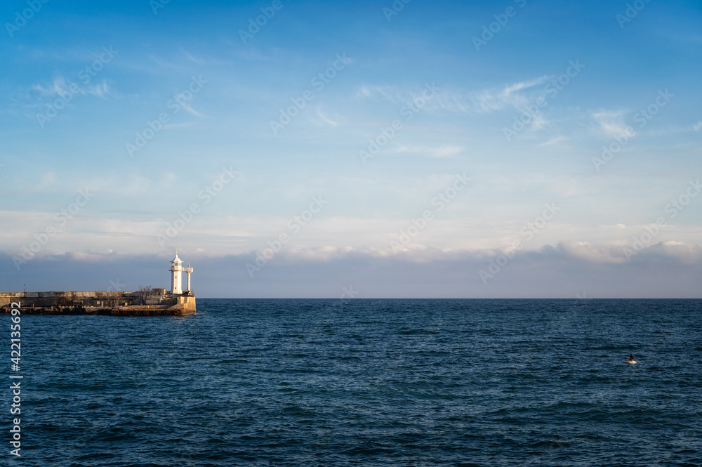 Lone beacon guards the ships. The lighthouse shows the way for boats. Calming scene. The gaze goes beyond the horizon