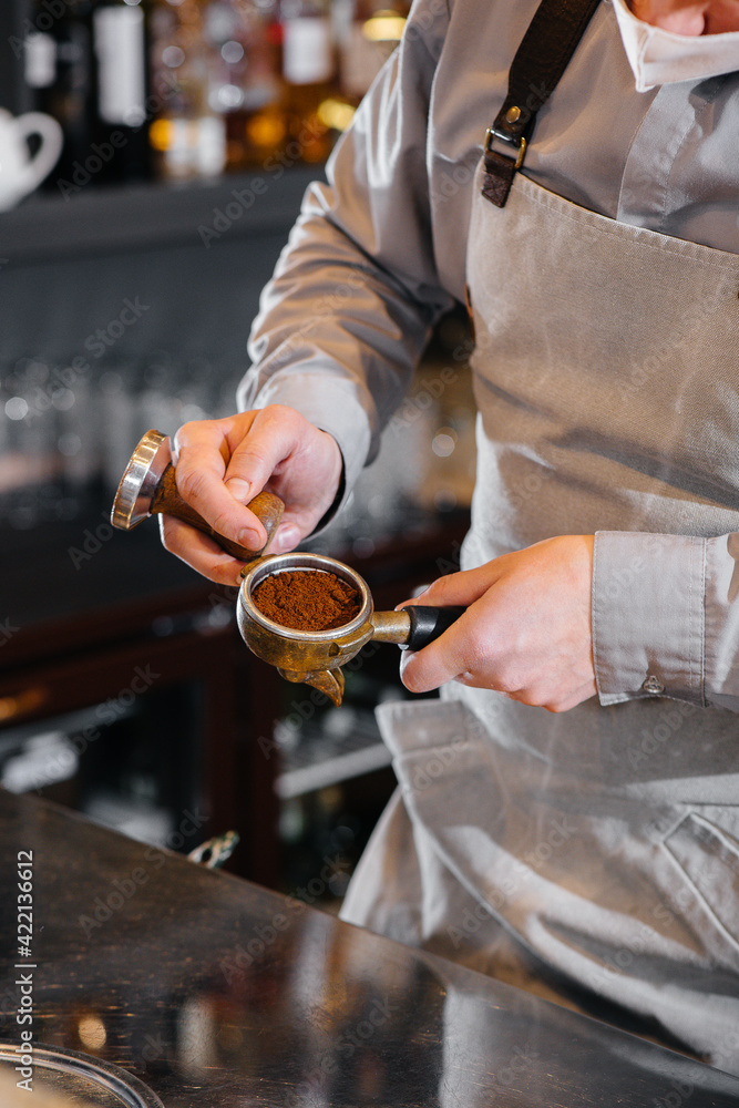 Close-up of a masked barista preparing a delicious coffee at the bar in a cafe. The work of restaurants and cafes during the pandemic.