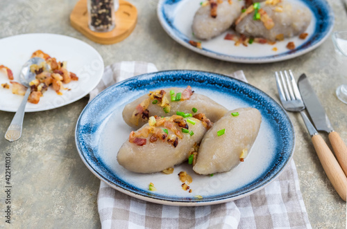 Traditional Lithuanian dish Zeppelin, boiled potato dumplings stuffed with minced pork, on a colored ceramic plate on a gray concrete background.