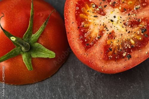 cut tomato with pepper and salt on a black slate background © SLindenau