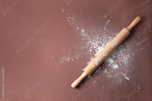 Wooden rolling pin in wheat flour on a brown background.