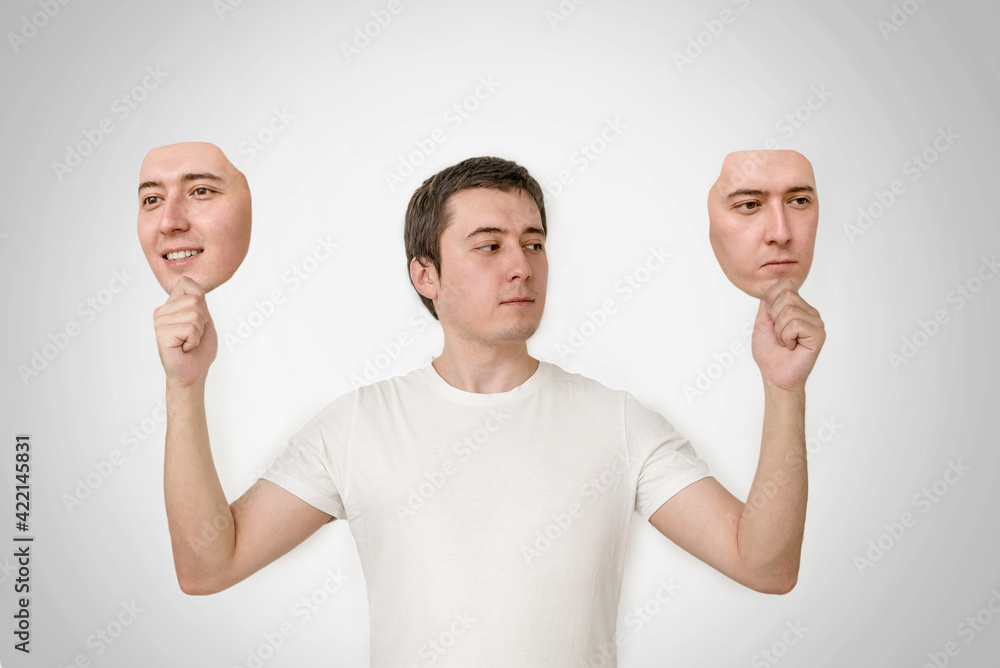 bipolar personality disorder. split personality, two-faced person. a man  holds two face masks in his hands. Stock Photo