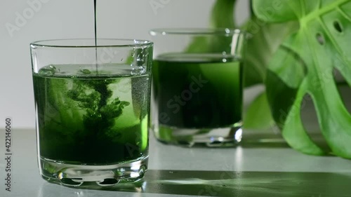 Chlorophyll extract is poured in pure water in glass against a white grey background with green leaf. Liquid chlorophyll in a glass of water. Concept of superfood, healthy eating, detox and diet photo