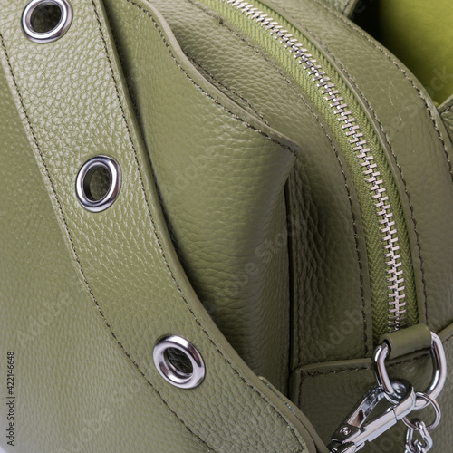 Close up of details of bag for women, made of genuine grained olive-colored leather. Handle with grommets. Zip closure