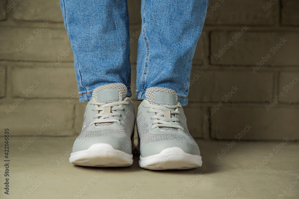 A woman in white sneakers stands against a brick wall in the background.