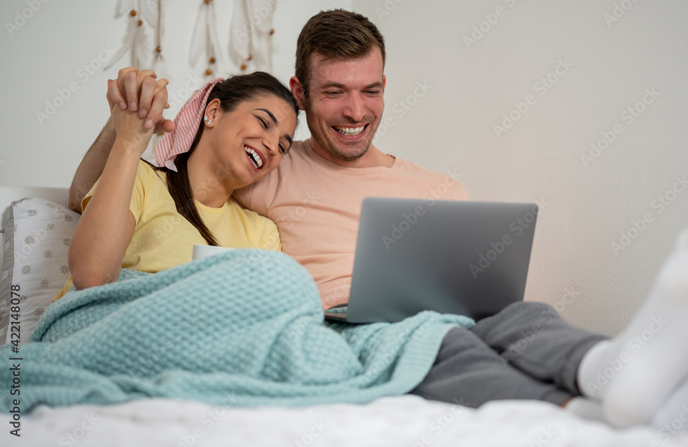 Happy young couple in love using a laptop and smiling in the bed in the bedroom. Happy young couple in love using a laptop and smiling in the bed in the bedroom.