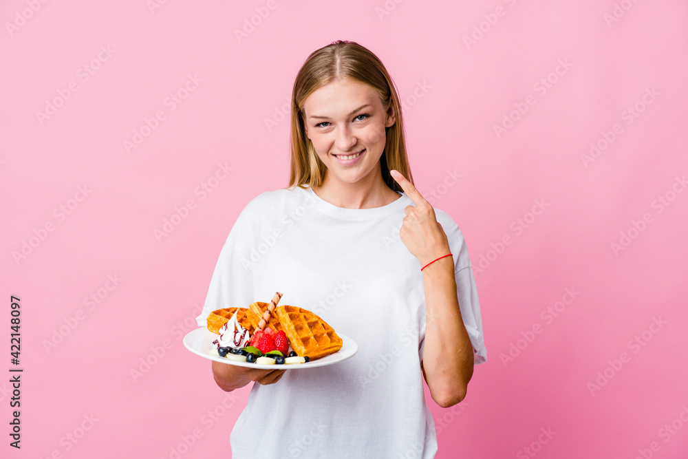 Young russian woman eating a waffle isolated smiles, pointing fingers at mouth. Young russian woman eating a waffle isolated smiles, pointing fingers at mouth.
