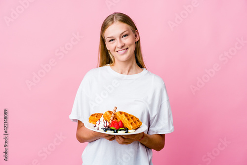 Young russian woman eating a waffle isolated happy, smiling and cheerful.
