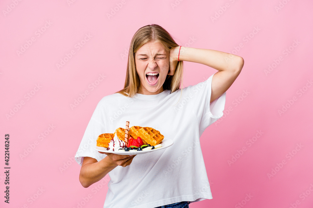 Young russian woman eating a waffle isolated covering ears with hands trying not to hear too loud sound.