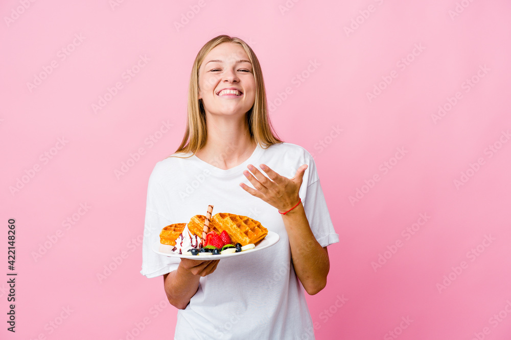 Young russian woman eating a waffle isolated laughs out loudly keeping hand on chest. Young russian woman eating a waffle isolated laughs out loudly keeping hand on chest.