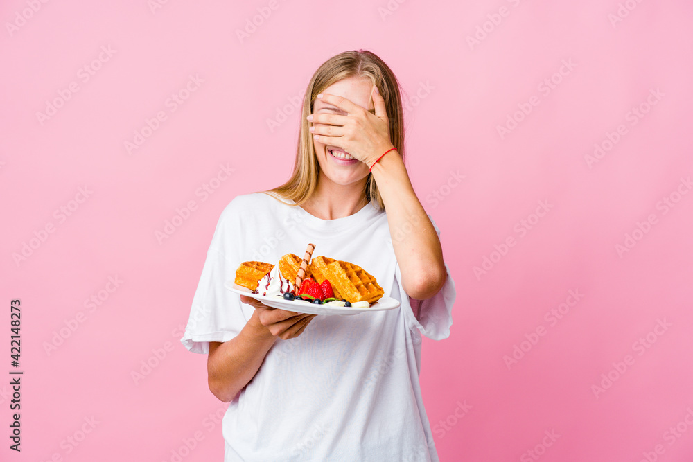 Young russian woman eating a waffle isolated covers eyes with hands, smiles broadly waiting for a surprise. Young russian woman eating a waffle isolated covers eyes with hands, smiles broadly waiting for a surprise.