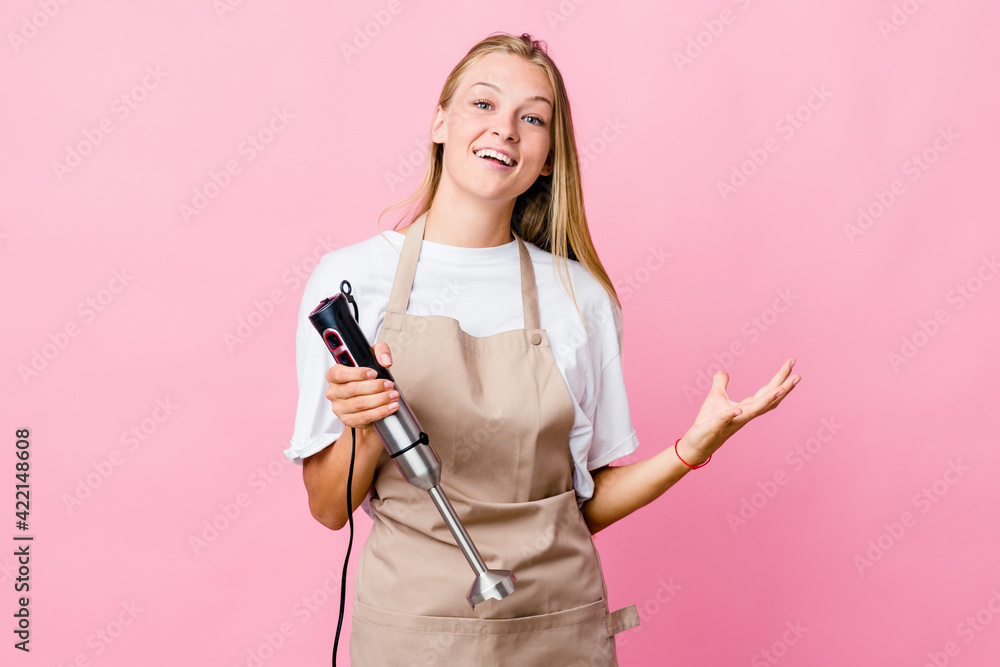 Young russian cook woman holding an electric mixer isolated celebrating a victory or success, he is surprised and shocked.