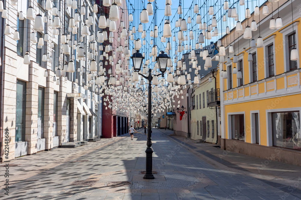 Decorations of Stoleshnikov lane in Moscow. Large garland from electric bulbs hangs above pedestrian street. Clear blue sky in the background. Travel in Russia theme.