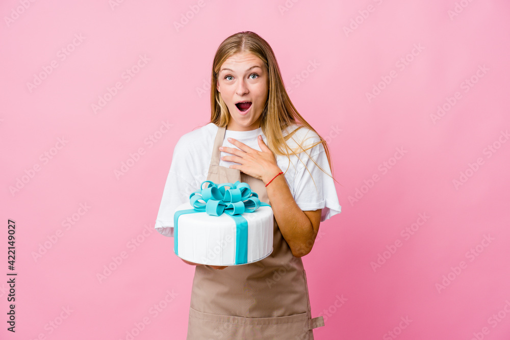 Young russian baker woman holding a delicious cake praying for luck, amazed and opening mouth looking to front. Young russian baker woman holding a delicious cake praying for luck, amazed and opening mouth looking to front.
