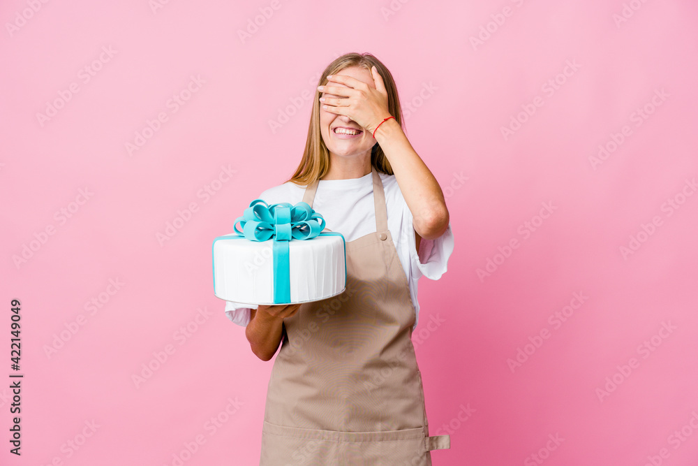 Young russian baker woman holding a delicious cake covers eyes with hands, smiles broadly waiting for a surprise. Young russian baker woman holding a delicious cake covers eyes with hands, smiles broadly waiting for a surprise.
