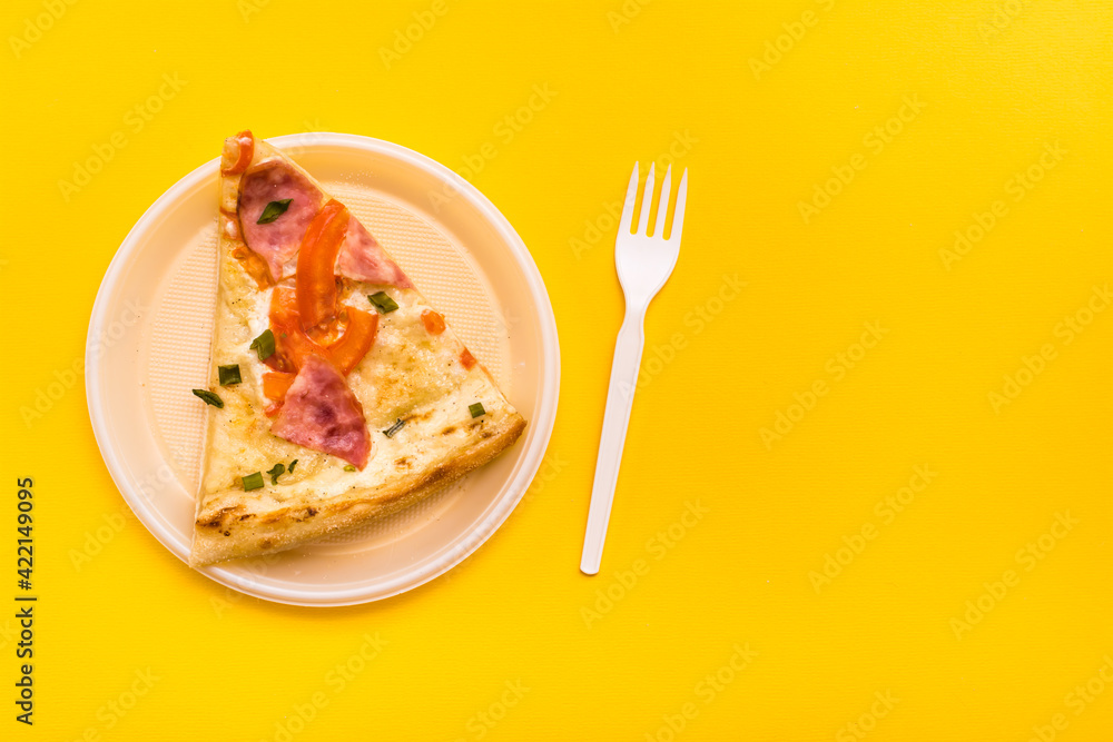 Takeaway and delivery. Pizza slice in disposable plastic plate and fork on yellow background Takeaway and delivery. Pizza slice in disposable plastic plate and fork on yellow background