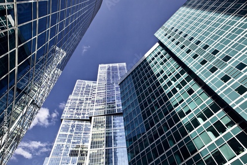 Office and residential skyscrapers against bright sun and clear blue sky close up. Reflections and glare on the glass facades of modern skyscrapers close-up. Modern buildings exterior design. 