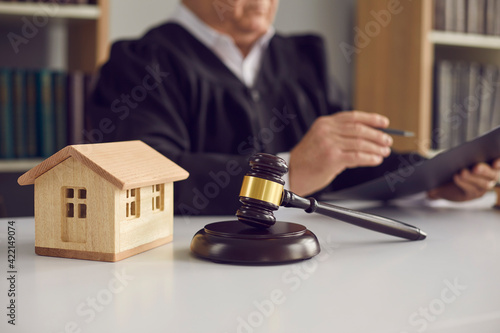 Close-up of judge's gavel, sound block, and small wooden toy house on courtroom table in court. Concept of real estate law, partition of property, separation of estates and divorce settlement