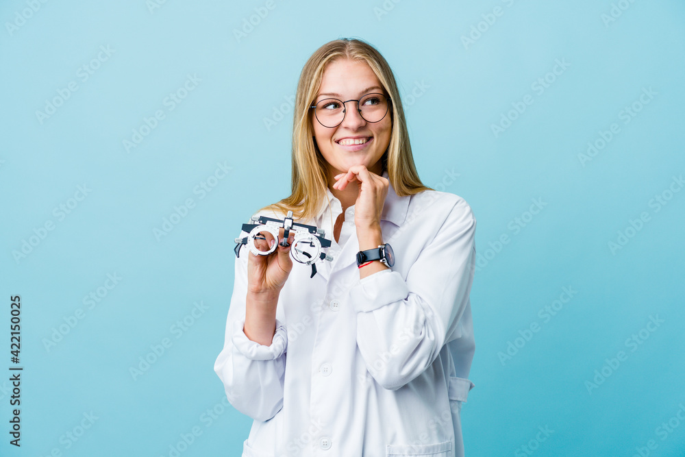 Young russian optometrist woman on blue keeps hands under chin, is looking happily aside. Young russian optometrist woman on blue keeps hands under chin, is looking happily aside.