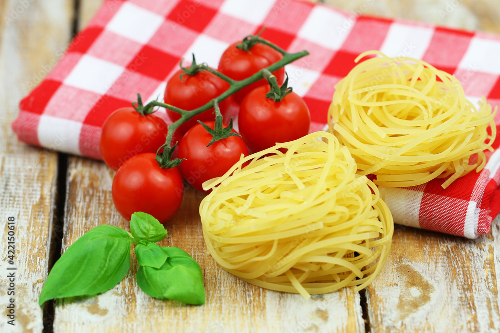 Uncooked pasta, fresh basil leaves and cherry tomatoes on checkered cloth