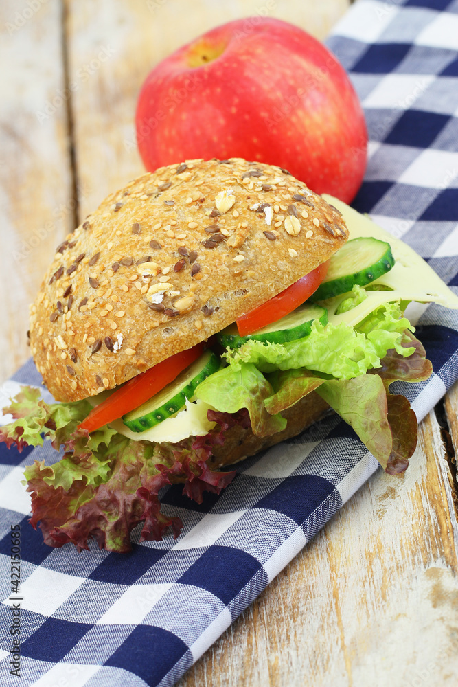 Lunchbox containing whole grain roll with Swiss cheese, lettuce and cucumber and red apple