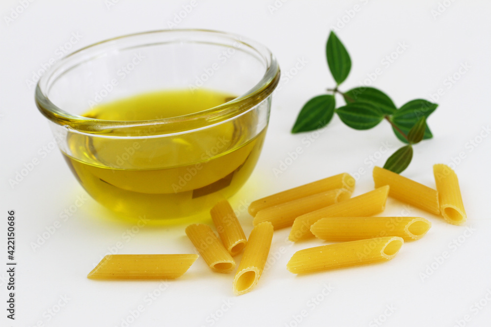 Olive oil in glass bowl and uncooked penne rigate pasta