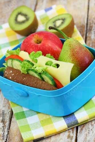 Healthy lunch box with whole grain roll with Swiss cheese, lettuce, tomato and cucumber; apple and kiwi fruit
