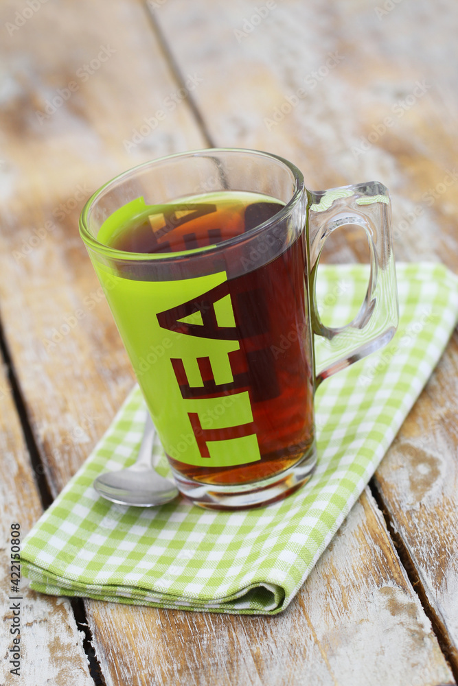 Black tea in transparent glass on checkered cloth on rustic wooden surface