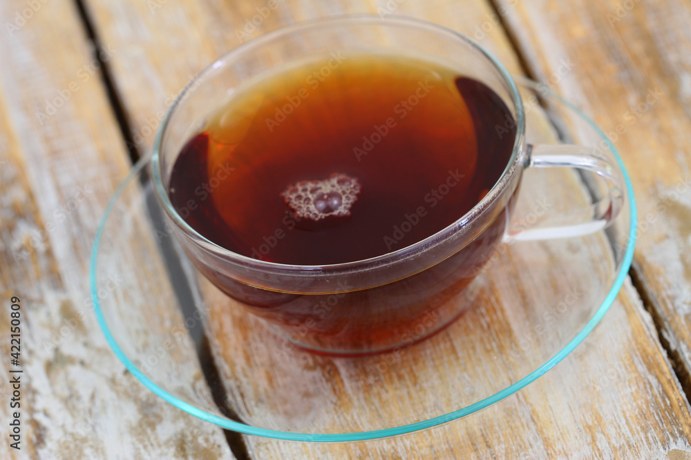 Tea in transparent cup on transparent saucer on rustic wooden surface
