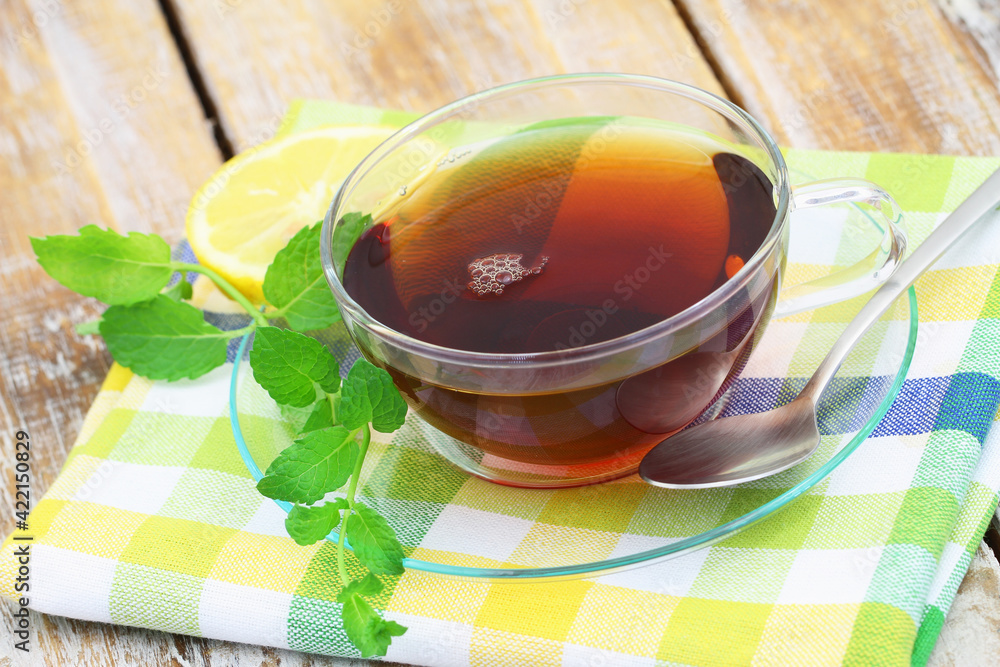 Tea in transparent cup, fresh mint leaves on rustic wooden surface