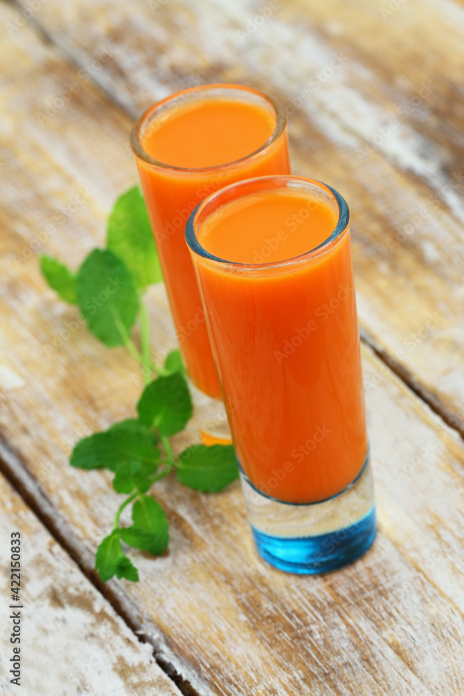 Freshly made carrot juice in thin transparent glasses on white surface, closeup