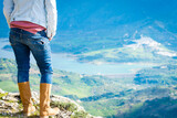 Mujer con botas y jeans, observando el paisaje en la montaña