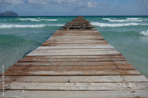 Long wooden pier entering into the wavy sea on a sunny day in Alcudia  Mallorca