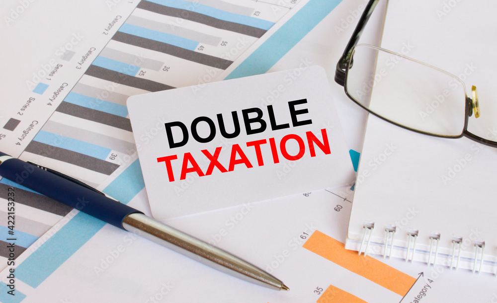 Business card with text Double Taxation lies on financial charts with pen and eyeglass Business card with text Double Taxation lies on financial charts with pen and eyeglass