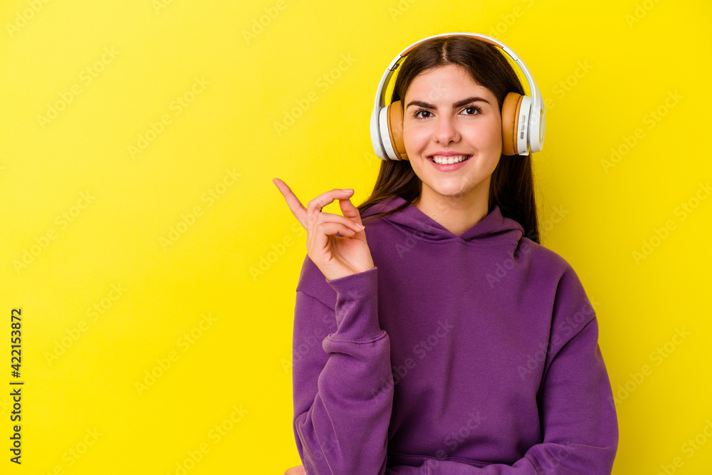 Young caucasian woman listening to music with headphones isolated on pink background smiling cheerfully pointing with forefinger away.