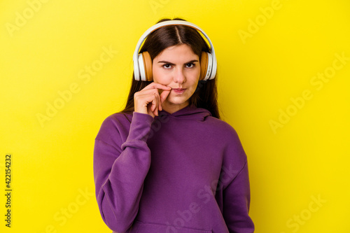 Young caucasian woman listening to music with headphones isolated on pink background with fingers on lips keeping a secret.