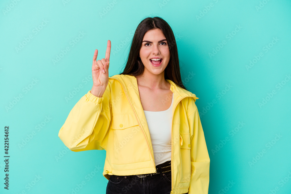 Young caucasian woman isolated on blue background showing rock gesture with fingers Young caucasian woman isolated on blue background showing rock gesture with fingers