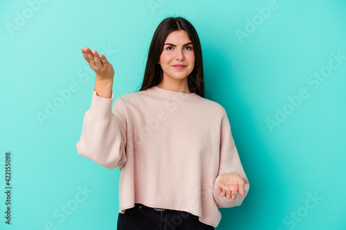 Young caucasian woman isolated on blue background makes scale with arms, feels happy and confident.