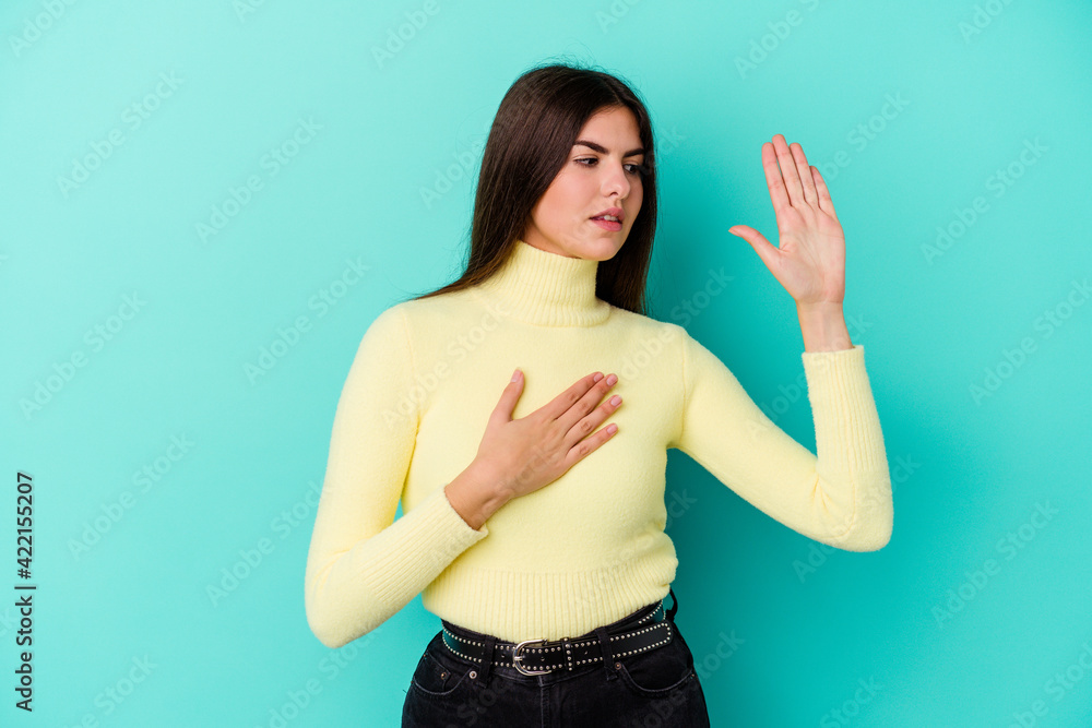 Fototapeta premium Young caucasian woman isolated on blue background taking an oath, putting hand on chest.