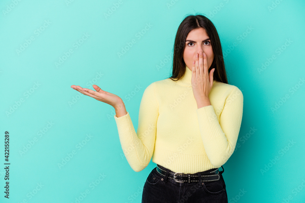 Young caucasian woman isolated on blue background impressed holding copy space on palm. Young caucasian woman isolated on blue background impressed holding copy space on palm.
