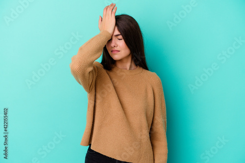 Young caucasian woman isolated on blue background forgetting something, slapping forehead with palm and closing eyes.