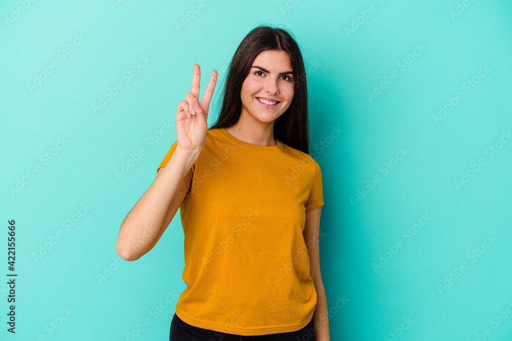Young caucasian woman isolated on blue background joyful and carefree showing a peace symbol with fingers. Young caucasian woman isolated on blue background joyful and carefree showing a peace symbol with fingers.