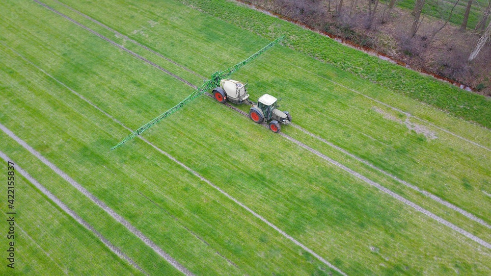 Traktor mit Spritze versprüht Pflanzenschutzmittel auf einem Acker, industrielle Landwirtschaft aus der Vogelperspektive Traktor mit Spritze versprüht Pflanzenschutzmittel auf einem Acker, industrielle Landwirtschaft aus der Vogelperspektive