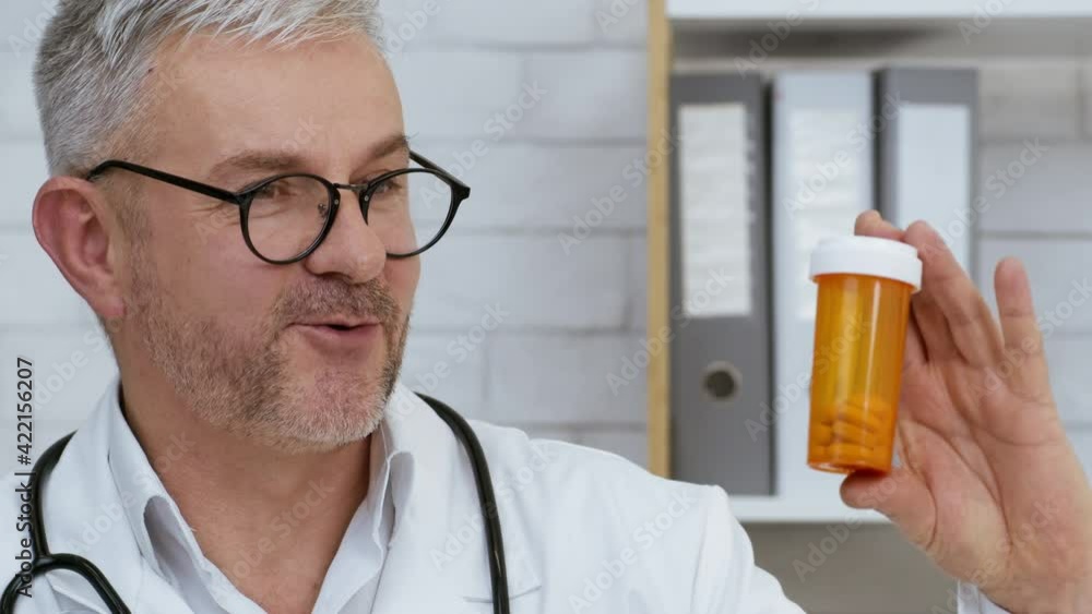 Male Doctor Showing Medical Pills Tube Recommending Medication In Clinic Male Doctor Showing Medical Pills Tube Recommending Medication In Clinic
