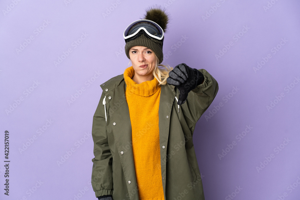 Skier Russian girl with snowboarding glasses isolated on purple background showing thumb down with negative expression