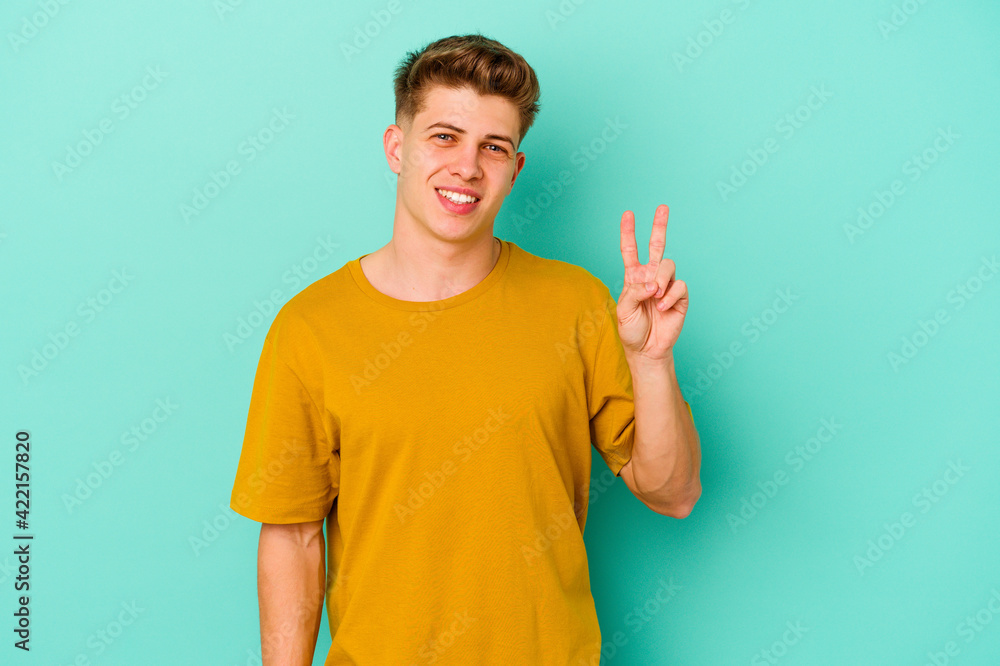 Fototapeta premium Young caucasian man isolated on blue background showing victory sign and smiling broadly.