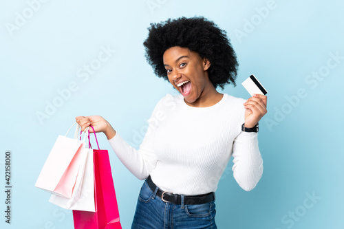 Young African American woman isolated on blue background holding shopping bags and a credit card
